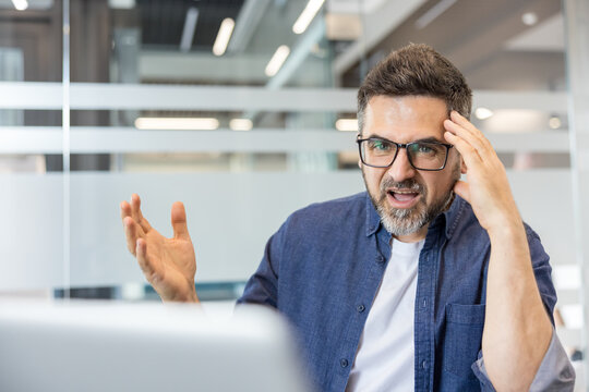 Angry man gesturing while having a heated video call or conversation, expressing frustration and burnout during a stressful situation in a corporate workplace