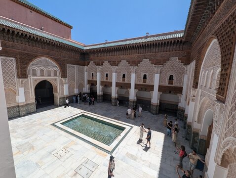 Courtyard of Riad Dar Lalla F'dila in Marrakesh, Morocco, with intricate zellij tilework, arches, and turquoise roofs under a bright summer sky.