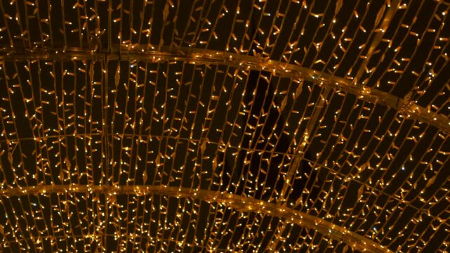 Golden twinkling string lights abstract background. Golden lights on a string blinking and creating a bokeh effect on a dark background. Christmas decorations inside a tunnel creating an abstract