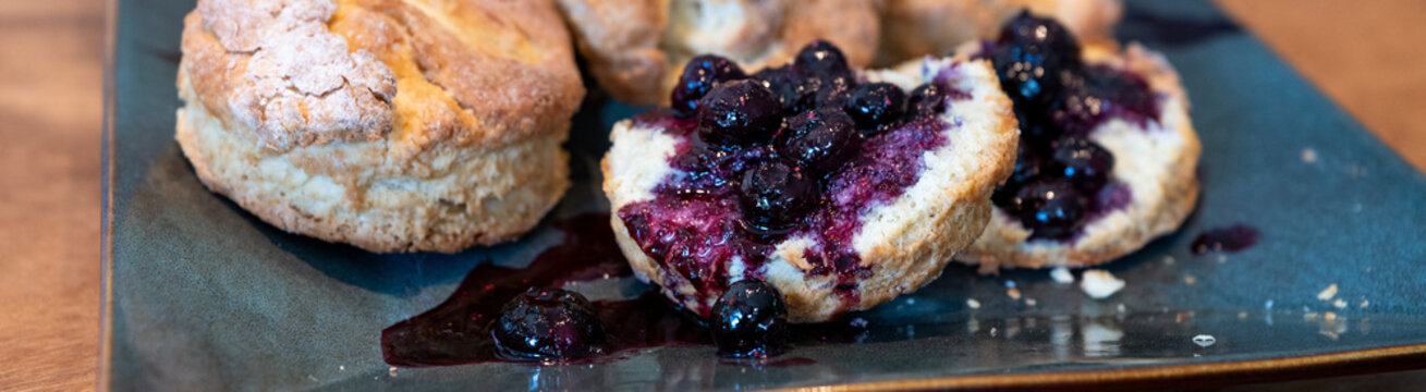 Homemade biscuits on a square platter, split open and topped with hand crafted blueberry sauce, delicious summer food treat
