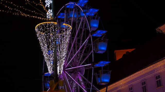 Colorful ferris wheel spinning at christmas market. Luminous ferris wheel rotating against a dark night sky with beautiful christmas decorations in the foreground