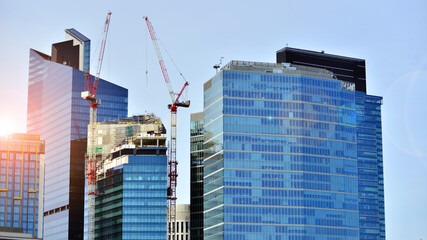 Fototapeta premium Crane on the construction site in a site surrounded by the high buildings. Office building under construction in the vicinity of high apartment buildings and office building.
