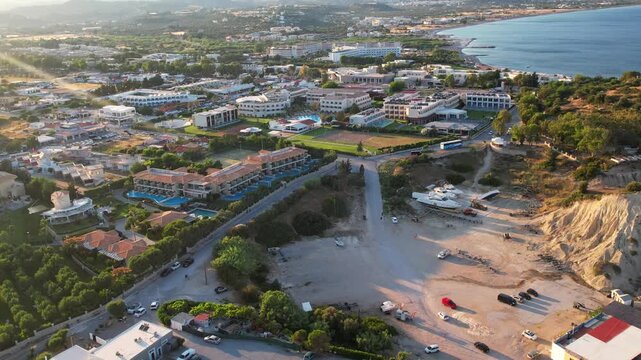 Cinematic aerial drone view of Kolymbia resort town on Rhodes island, Greece. The footage showcases luxury hotel complexes with swimming pools and tennis courts, roads, lush gardens