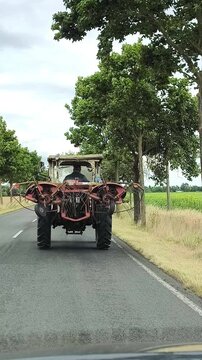 An old tractor with a hay tedder is driving along an asphalt road.