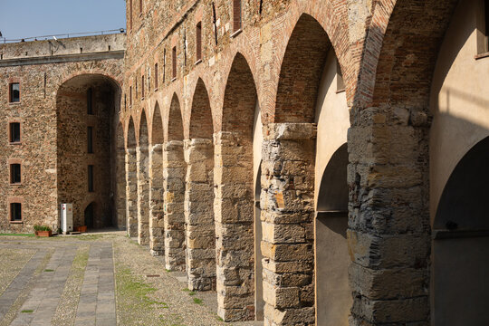 Interior view of the courtyard of the Medieval Fortress with Stone Arches of Priamar in Savona, Liguria, Italy. Close-up of an ancient fortified courtyard with a rustic stone arched gallery, medieval