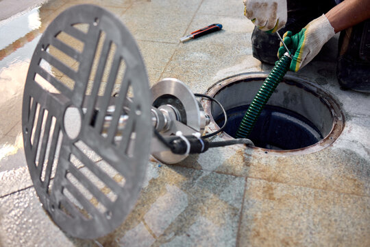 removal of manhole cover on sidewalk with concrete and metal materials, practical ground-level view, gray and green tones, utility maintenance in construction setting.
