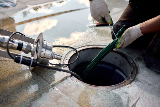 removal of manhole cover on sidewalk with concrete and metal materials, practical ground-level view, gray and green tones, utility maintenance in construction setting.