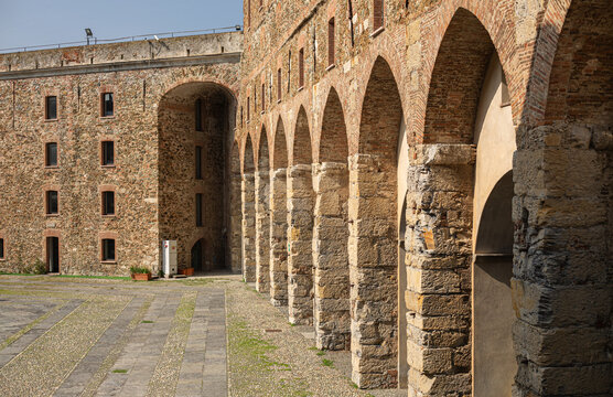 Interior view of the courtyard of the Medieval Fortress with Stone Arches of Priamar in Savona, Liguria, Italy. Close-up of an ancient fortified courtyard with a rustic stone arched gallery, medieval