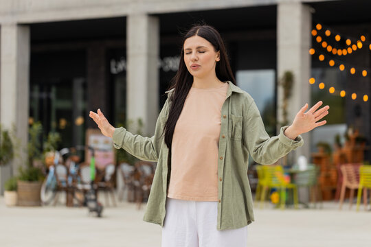 Young woman calming down walking in city street with deep breath after stressful work. Girl tourist meditating outdoors and calming mind with breathing practice after tension near busy office center.