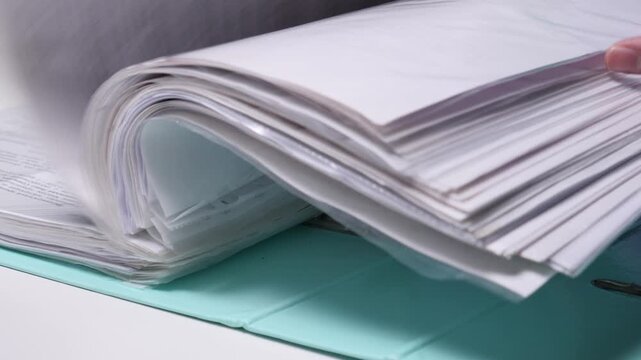 Person's hand flipping through a thick binder filled with numerous white paper documents, representing concepts of administration, records, and extensive paperwork management