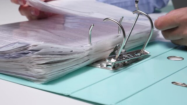 Person's hands are actively filing or retrieving important papers from a large, overflowing ring binder, representing administrative tasks and the process of managing extensive paperwork