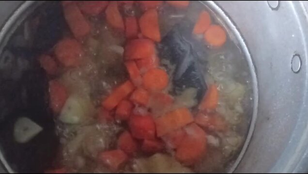 Carrot soup with clear broth, cooked in a pot until boiling.