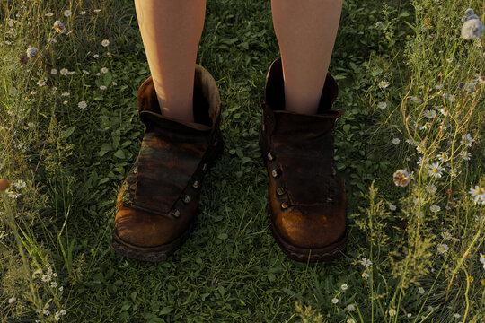 3D rendering of old leather hiking boots with feet standing in a meadow in the summer