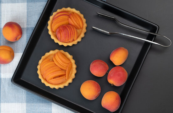 A top view of tartlets shaped like small apricot cakes. Ripe apricots lie next to them.