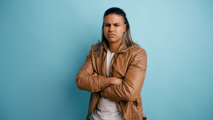 Obraz premium Latino man with long hair standing crossing arms, looking at camera with a skeptical and serious expression