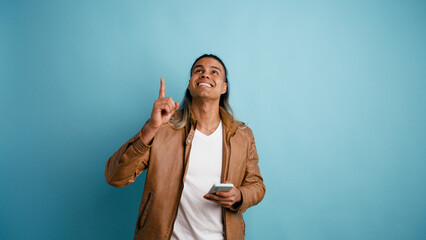 Smiling latino man pointing finger up, having a good idea, innovation or creative thought, presenting new solution © DMegias