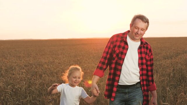 Happy family father farmer and little daughter walking at sunset dry wheat field closeup. Smiling man parent and cute girl kid child holding hands talking enjoy farming outdoor leisure with love