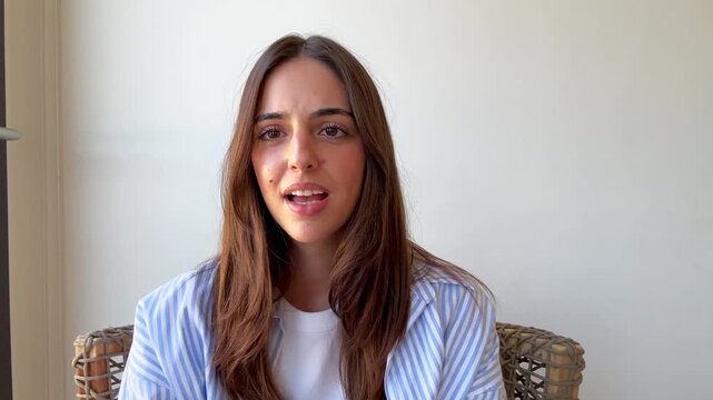 A young woman with long brown hair speaks directly to the camera, then transitions to a serious, thoughtful expression. Her changing emotions convey a narrative of communication and contemplation.