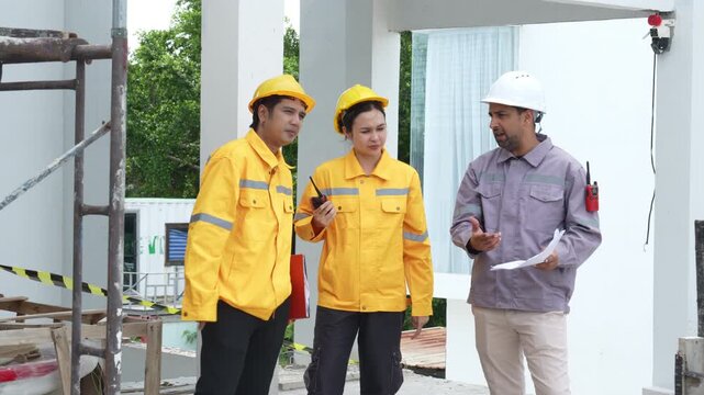 Construction engineers in safety helmets inspecting a residential building exterior, reviewing site progress, scaffolding and project management during an on-site construction inspection.