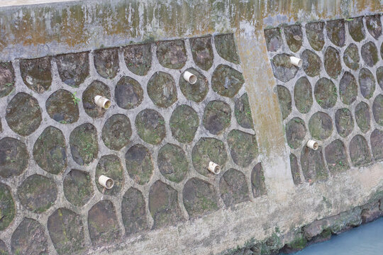 Concrete retaining wall structure with drainage pipes and stone pattern texture
