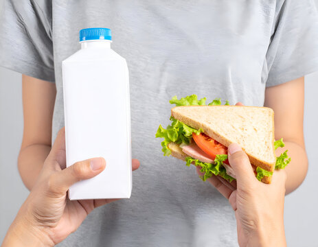 Person holding a blank white carton and a ham sandwich, healthy lunch meal in hands, isolated on gray, minimalist snack or drink product mockup, casual lifestyle.