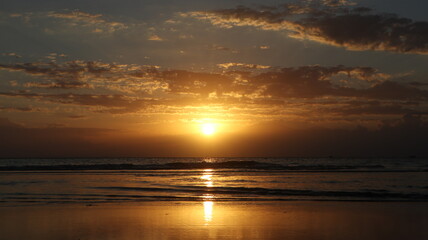 Obraz premium Golden Coastal Sunset: The sun glows intensely as it sinks toward the horizon, casting a shimmering reflection across the calm ocean waves in the background