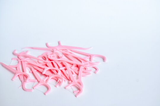 A group of pink plastic dental floss picks arranged on the lower side of a white background with negative space.