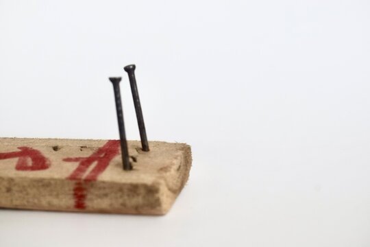 Studio shot focusing on two metallic nails driven vertically into a small wooden block marked with red ink against a white background.
