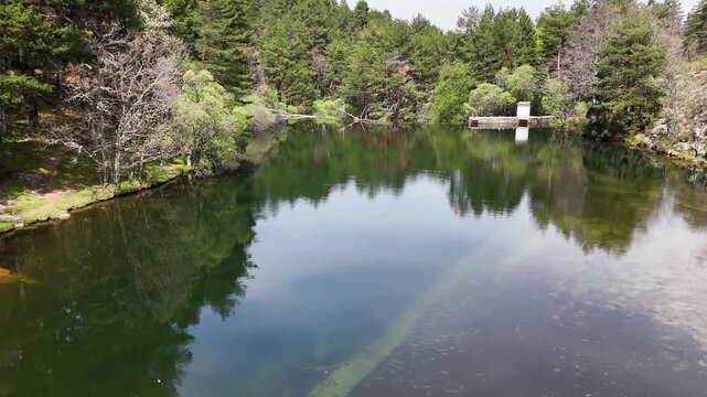Aerial drone footage of the calm reservoir at Presa del Pradillo on the Rio Manzanares in El Pardo, Madrid, Spain, with reflections of pine forest and granite rocks