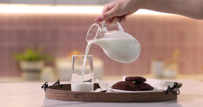 Woman pouring fresh milk into glass at table in kitchen, closeup. Camera moving forward