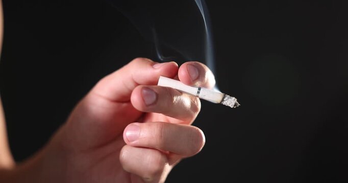 Man holding burning cigarette on black background, closeup