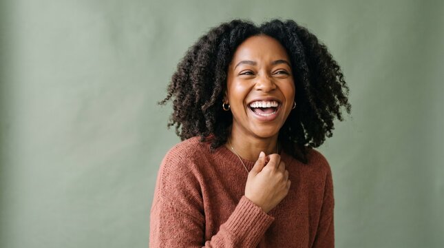 Smiling Black woman with curly hair in rust sweater, sage green background