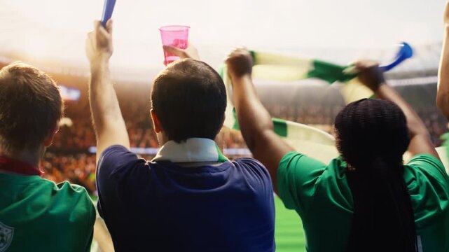 Rear view of football supporters holding drink cup while facing pitch, waving scarves for fan culture, stadium atmosphere and team support content.