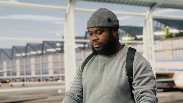 Close up of joyous man in airport excited to go on holiday trip, passing by plane on runway, relaxed African American traveler enthusiastic about vacation, going to flight boarding gate.