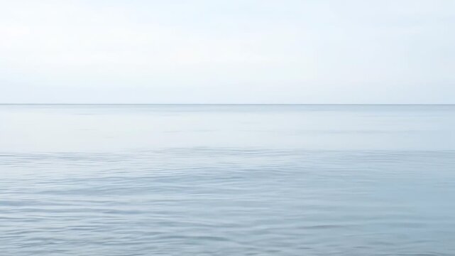 Soft, subtle blue ocean waves meet the hazy sky in this tranquil seascape image