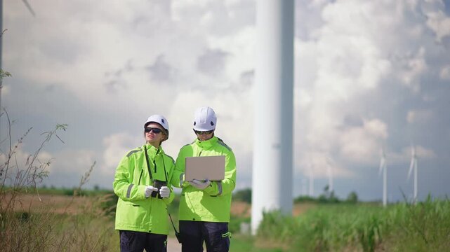 Wind energy engineers inspecting a wind farm, discussing renewable power, turbine maintenance, teamwork and sustainable energy in an outdoor environment.