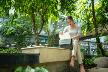 Fototapeta premium Woman Working Outdoors with Laptop Amid Lush Greenery in Urban Space
