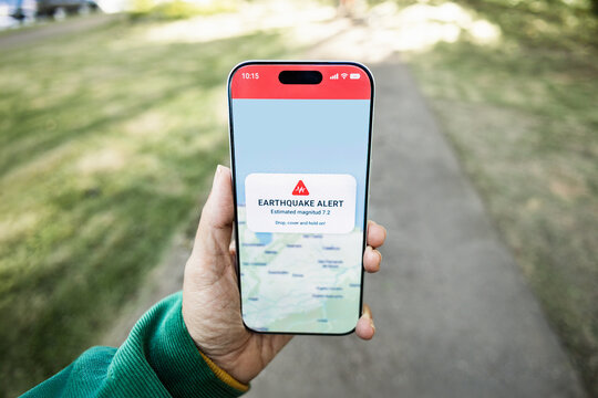 Person using earthquake app on mobile phone for real-time emergency alert - High magnitude warning
