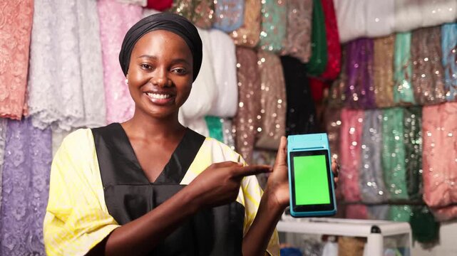 African woman entrepreneur holding a pos terminal with green screen for payment in her fabric shop