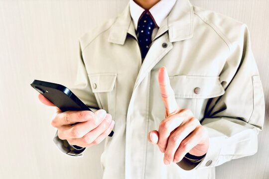スマホを持って人差し指を立てる作業員