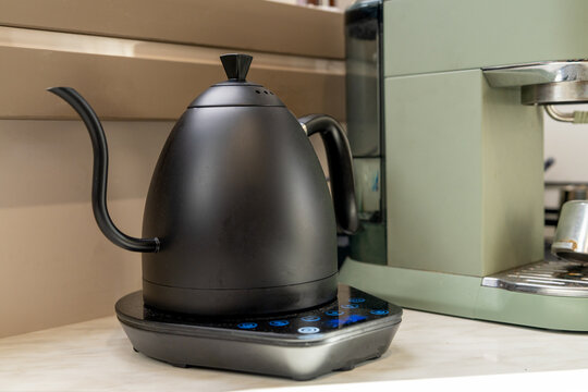 Modern black gooseneck electric kettle on a digital scale next to a green espresso machine in a stylish home coffee corner