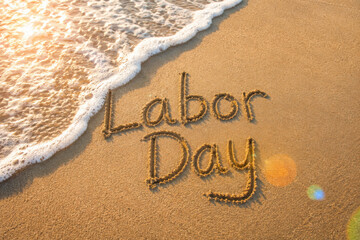 Labor Day message handwritten on the smooth sand of an empty beach with sunny lens flare across an oncoming wave