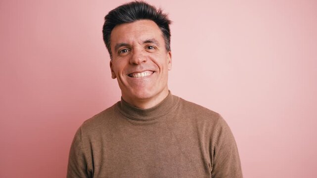 Handsome and cheerful middle aged man expressing genuine happiness. His face radiates positivity as he smiles and laughs against a pink background