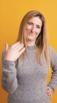 Confident and attractive woman with blonde hair gesturing to come here. Playful and flirty invitation with a smirk against a yellow background. Vertical