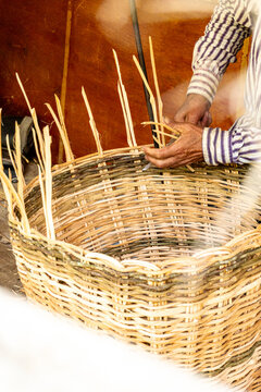 Senior male artisan weaving a traditional wicker basket by hand in a rustic workshop, close-up of skilled hands crafting authentic handmade rattan products