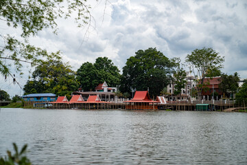 Floating fish feeding rafts with traditional Thai pavilions along the riverside of Wat ThaSung, viewed from across the river with lush green trees in the background. © Surachetsh