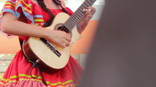 An unrecognizable woman in traditional dress plays a tiple during a live performance at the San Juan and San Pedro Festival in Neiva, Huila, Colombia. Concept of Colombian music and folklore