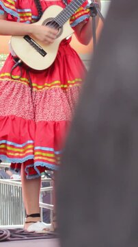 An unrecognizable woman in traditional dress plays a tiple during a live performance at the San Juan and San Pedro Festival in Neiva, Huila, Colombia. Concept of Colombian music and folklore