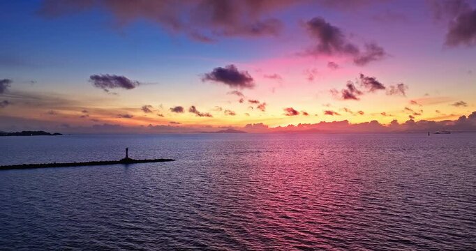 Dramatic sunrise sky with purple and orange clouds over the calm sea and the silhouette of a lighthouse in Zhuhai, China