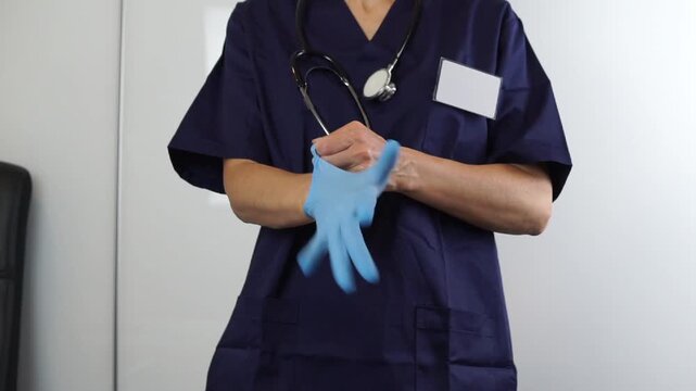 Mid-section of a healthcare worker wearing a stethoscope and putting on blue sterile gloves before a medical procedure, ensuring safety and hygiene protocols.